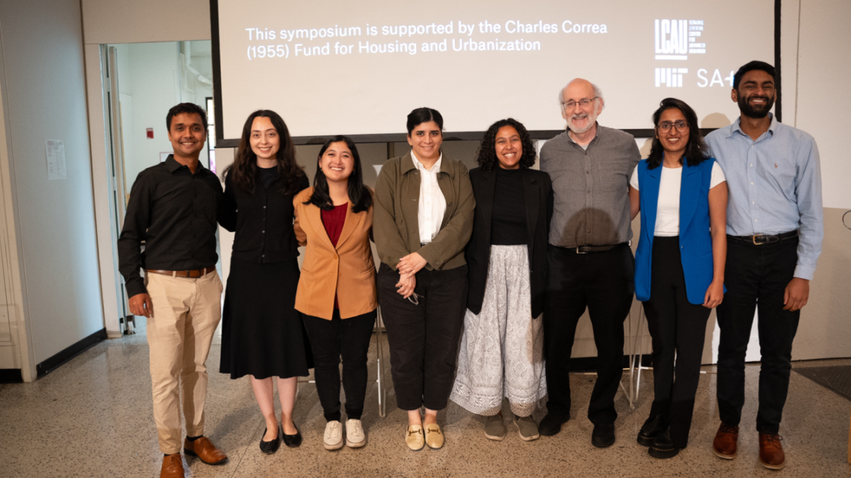 Students and instructors from the course smile in front of a screen from the course symposium.