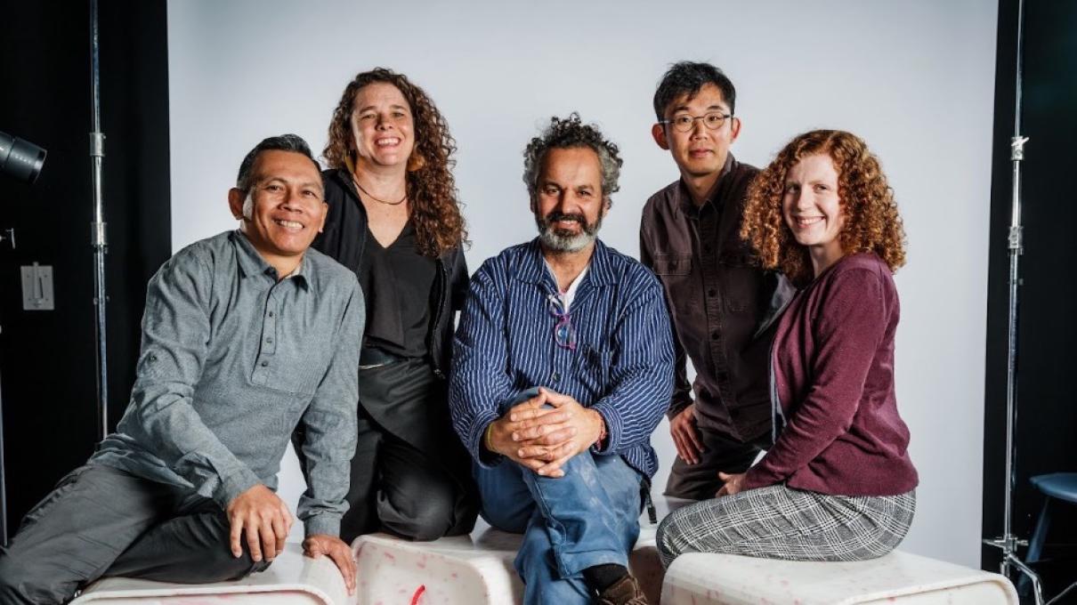 Five individuals seated and surrounding small benches made of white and pink recycled material and with pink ropes attached.